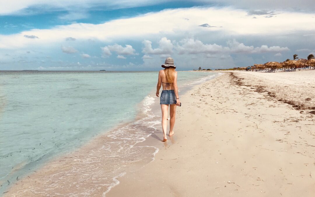 κοπέλα με τζιν σορτσάκι και μαγιό περπατάει στην παραλία