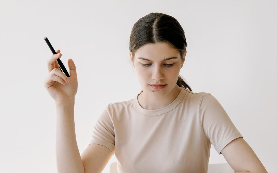 κοπέλα που έχει μπροστά της σε γραφείο κινητό, μπλοκ σημειώσεων, χαρτιά και κρατάει στο δεξί της χέρι στυλό.