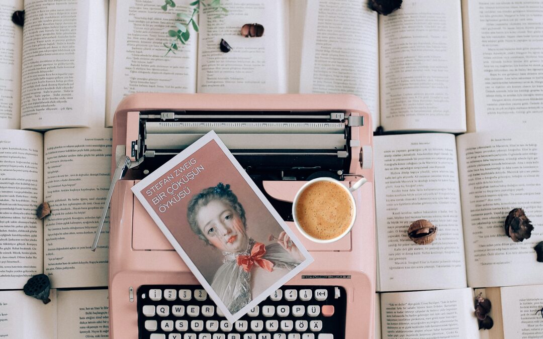 Ροζ γραφομηχανή, καφές, μια εικόνα κοριτσιού, πολλά βιβλία κάτω απο τη γραφομηχανή και ένα λουλούδι σε κάθε ανοιχτό βιβλίο.