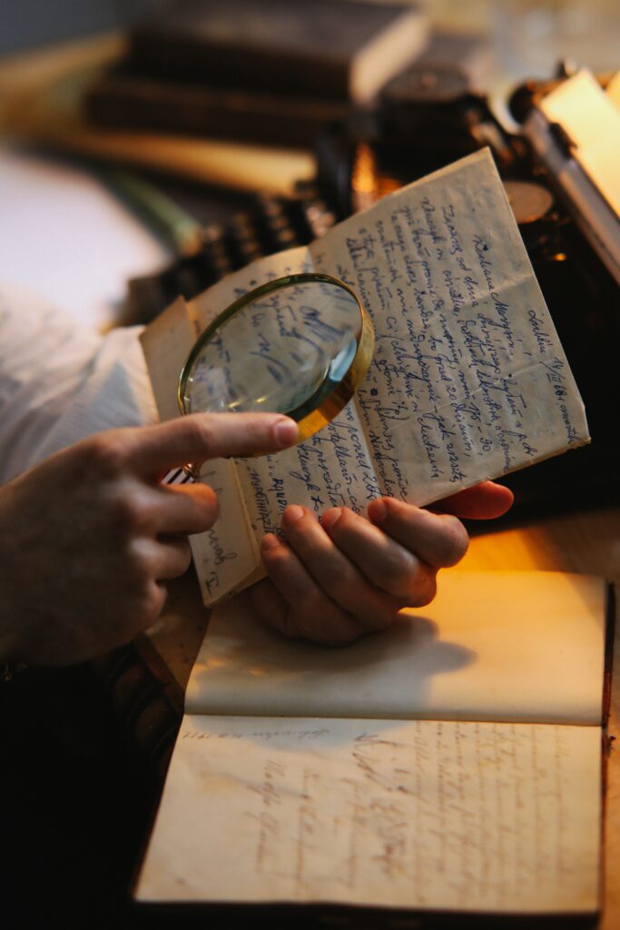 Συμβουλές για επαγγελματική κειμενογραφία από την Ευαγγελία Ξώνη. Ένα χέρι κρατά μεγεθυντικό φακό επάνω από χειρόγραφο χαρτί. 